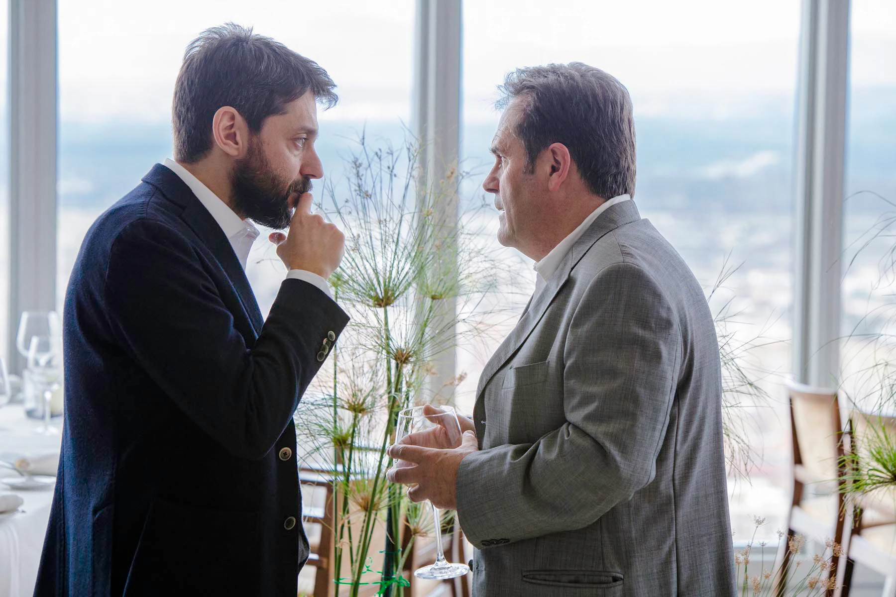 Dos directivos conversando durante momento de networking en evento corporativo en rascacielos de Madrid, con copa de vino y ambiente profesional
